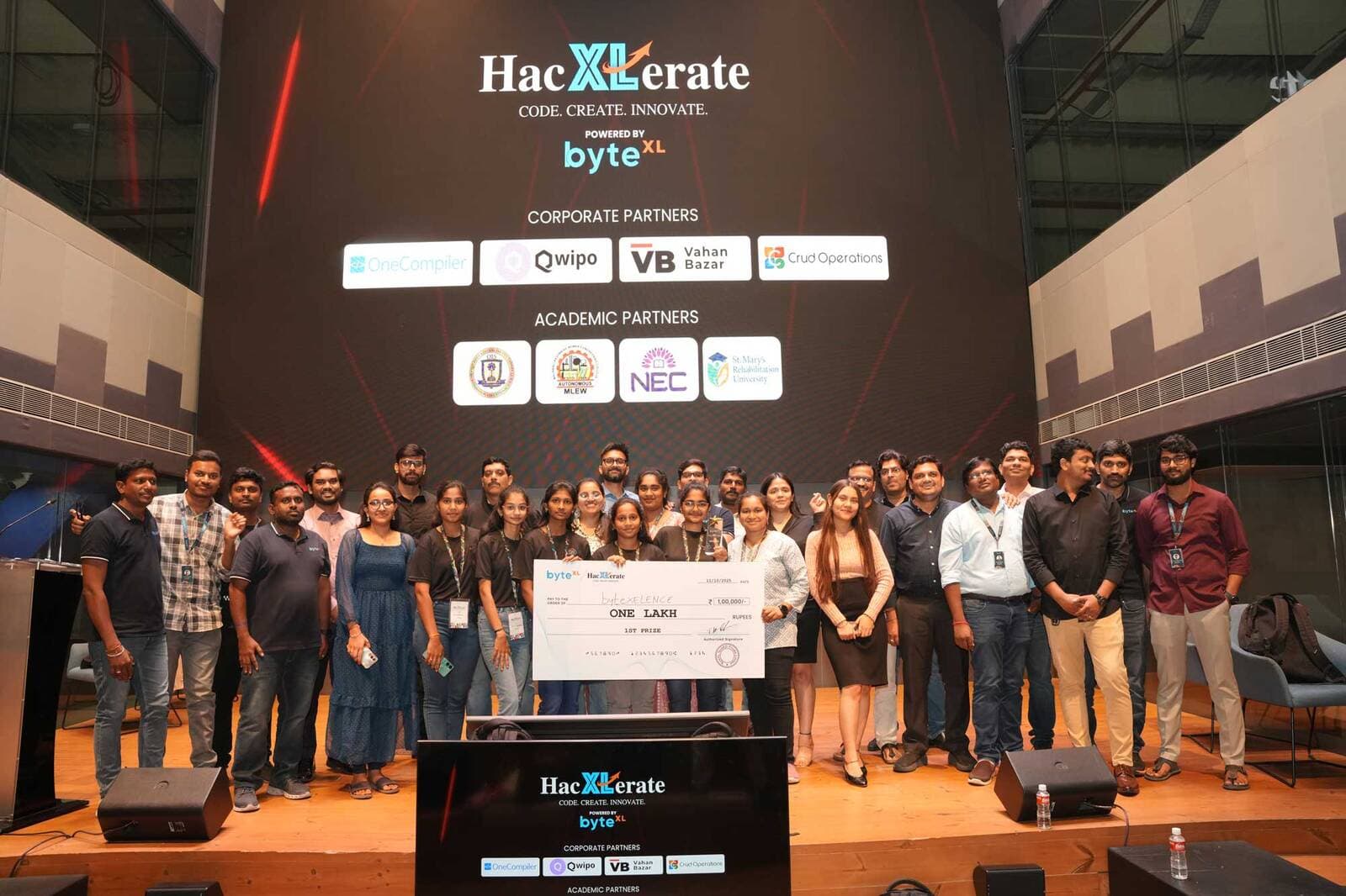 A winning team receiving a ₹1,00,000 prize cheque on the HacXLerate stage